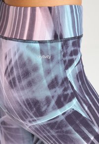 Leggings de talle alto en una mezcla de gradientes azules y morados con patrones abstractos. Presentan una textura suave y detalles de costura en negro.