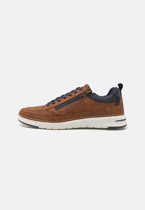 Braune lässige Sneaker mit marineblauen Schnürsenkeln, Reißverschlussdetails an der Seite, weißer Sohle und dunklem gepolstertem Kragen auf weißem Hintergrund.