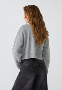 Korte grijze trui met een geribbelde zoom, gecombineerd met losse zwarte denimbroek met een elastische tailleband en achterzakken.