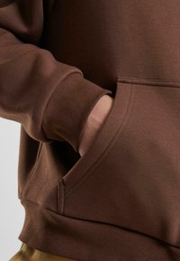 Brauner Baumwoll-Hoodie mit gerippten Bündchen und Saum, Kängurutasche mit seitlichem Zugang und weichem, strukturiertem Stoff.