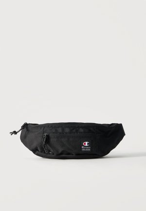 Riñonera negra de la marca Champion con bolsillo frontal con cremallera y parche con logo sobre fondo neutro.