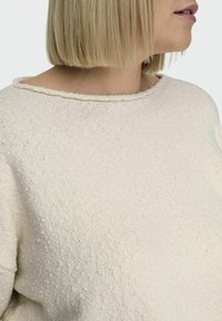 Pull en ivoire texturé avec un col ras du cou et des épaules tombantes, présentant un motif subtil à flocons et un tissu tricoté doux.