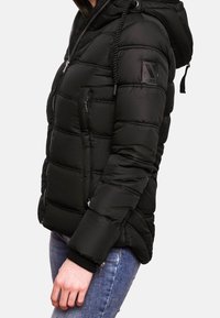 Svart puffjacka med huva, med quiltat mönster, dragkedjefickor, ribbstickade muddar och en logopatch på vänster ärm.