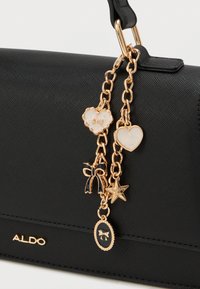 Borsa nera in materiale texturizzato, con hardware dorato e charm decorativi: cuori, un fiocco e una stella. Logo del marchio visibile.