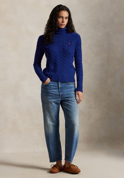 Blå kabelstrikket turtleneck-genser med ribbestrikket kant, kombinert med lyse vaskede cropped jeans og brune mokkasinstil-sko.