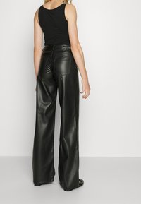 mustan nahka leveälahkeiset housut, joissa on sileä pinta, taka-taskut ja korkea vyötärö. Yhdistetty tiukkaan mustaan hihattomaan toppiin.