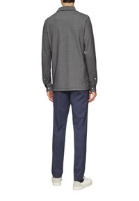 Graues Langarmhemd mit Kragen und Knopfmanschetten, kombiniert mit dunkelblauen Hosen und weißen Sneakers. Glatter Stoff, lässige Passform.