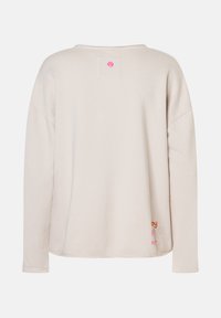 Beige Sweatshirt mit langen Ärmeln und lockerer Passform, kleinem rosa Rundlogo am Hals und buntem gesticktem Text sowie Herz am unteren Saum.