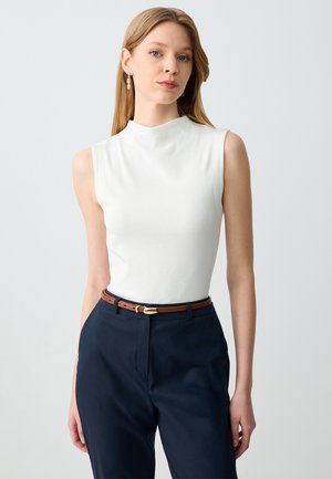 Haut sans manches blanc avec un col haut, associé à un pantalon navy et une ceinture marron avec une boucle en or. Texture lisse et design ajusté.