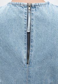 Πίσω όψη ενός ατόμου που φοράει ένα ανοιχτό μπλε τζιν ρούχο με κάθετο μαύρο φερμουάρ στο κέντρο.