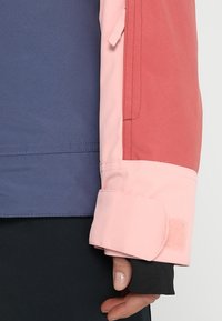 Kolorowa rękaw kurtki z niebieską górną częścią, różowym środkiem i koralowym akcentem; posiada rzep i gładką teksturę.