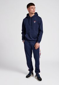 Navyblaues Hoodie- und Jogginganzugset aus Baumwolle. Das Hoodie hat eine Vordertasche und einen Kordelzug. Die Jogginghosen verfügen über seitliche Streifen und elastische Bündchen.