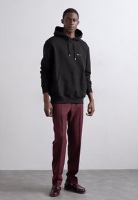 Sort bomulds hue med en kengurulomme, parret med maroon skræddersyede bukser og glansfulde burgunderrøde sko. Enkel design, ingen mønstre.
