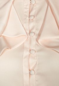 Hellrosa Bluse mit glatter Textur, Knopfverschluss vorne, Rüschensäumen und kleinen, stoffbezogenen Knöpfen.