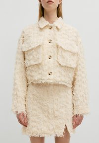 Crèmekleurige cropped jas met een rafelige textuur, borstzakken en knoopsluiting, gecombineerd met een bijpassende minirok met een zijschuif.