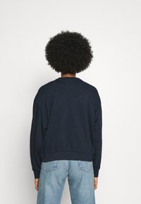 Felpa oversized blu navy con scollatura rotonda e polsini a coste, realizzata in tessuto morbido, abbinata a jeans azzurri.