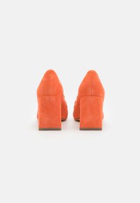 Orangemönstrade mockaklackar med tjock klack, spetsig tå och slät yta. Bakifrån syns rena linjer och en minimal design.