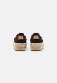Chaussures à plateforme noires en tissu avec des semelles d'esparto tressées couleur tan et des bords effilochés. Elles affichent une étiquette en cuir tan sur le talon.