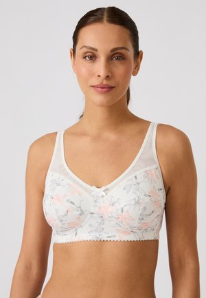 Donna con capelli castani raccolti che indossa un reggiseno bianco con motivo floreale con fiori rosa chiaro e grigi su sfondo semplice.