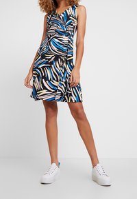 Musta mekko, jossa on värikäs siveltimenvetoikkunakuviota punaisessa, sinisessä ja keltaisessa. Siinä on hihaton, kietaisumalli ja se ulottuu polven ylle.