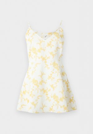 Valkoinen hihaton mekko ohuilla olkaimilla ja keltaisella kukkakuosilla, siinä on istuva yläosa ja levenevä hame.