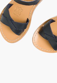 Meren laivasto nahkasandaalit, joissa on ristikkäiset hihnat, vaaleanruskea nahkapohja ja kontrastiväri valkoinen tikkaus reunoilla.