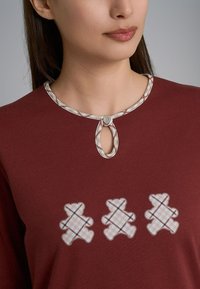 Top bordeaux con scollo a chiave e un bottone decorativo. Tre design di orsi ricamati in un colore chiaro con una texture a motivo.