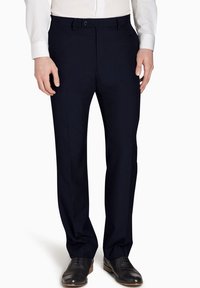 Marinehosen aus glattem Stoff, mit flachem Frontdesign, seitlichen Taschen und schmaler Passform, kombiniert mit dunklen Lederschuhen.