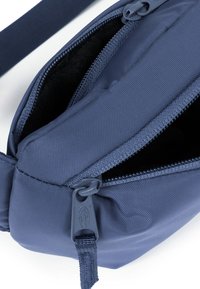 Borsa in nylon blu con due scomparti con zip, texture in tessuto e tracolla piatta. L'interno è foderato con materiale morbido per protezione.