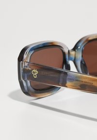 Oversized sunglasses with a gradient tortoiseshell frame, brown lenses, and gold logo detail on the temple. Smooth texture with rounded edges.