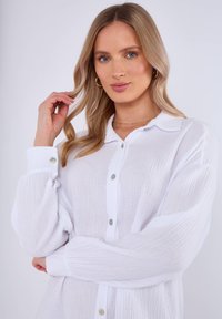 Chemise blanche à col boutonné avec un tissu texturé, dotée d'un col, de manches longues et de boutons vert clair.