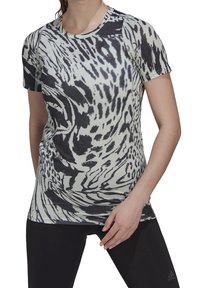 Kvinde iført en sort-hvid abstrakt mønstret Adidas kortærmet T-shirt og sorte Adidas leggings, poserende med den ene hånd på låret.