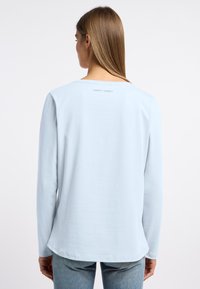 Lichtblauwe longsleeve shirt van zachte stof, met een ronde halslijn en een klein logodetail aan de achterkant nabij de nek.