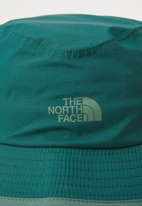Tirkizna kapa od laganog materijala, s ušivenim trakama i logotipom "THE NORTH FACE" u suptilnom zelenom printu s prednje strane.