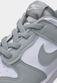 Κοντινό πλάνο του γκρι και λευκού αθλητικού παπουτσιού Nike που δείχνει τα κορδόνια, τις ραφές, το λογότυπο Nike και τη μαλακή γλώσσα με το λογότυπο.