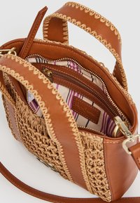 Bolso de cuero marrón con acentos de paja trenzada, que cuenta con un forro de tela a rayas y múltiples compartimentos, incluyendo un bolsillo con cremallera.