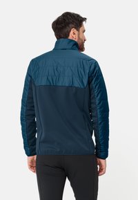 Blauwe lichtgewicht jas met een gequilt bovenrug, zacht materiaal,staande kraag en elastische manchetten, ontworpen voor comfort en bewegingsvrijheid.