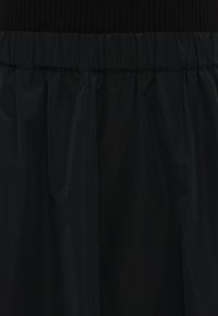 Svart skjørt med en samlet elastisk midje og et glatt, flytende design. Stoffet ser lett ut med en matt finish.