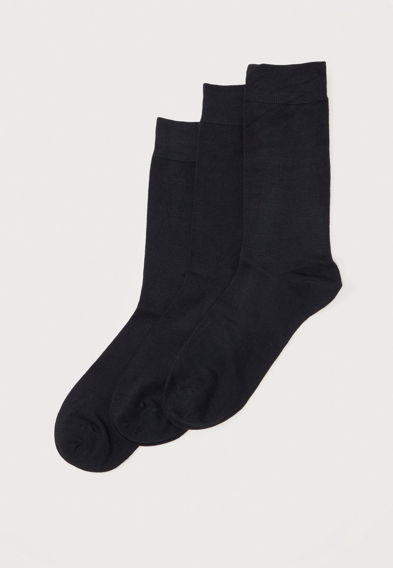 Trois paires de chaussettes noires unies de longueur classique empilées sur un fond blanc.