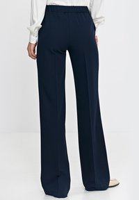 Granatowe spodnie o szerokich nogawkach z elastycznym pasem, gładkiego materiału, z bocznymi kieszeniami, zestawione z jasną bluzką.