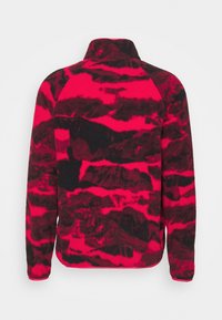Pullover in pile rosso e nero con colletto alto, caratterizzato da un motivo testurizzato che ricorda onde o montagne sulla stoffa.