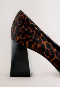 Scarpa con tacco a blocco stampa leopardata in pelliccia marrone e nera con tacco geometrico spesso in legno nero. Presenta una punta appuntita.