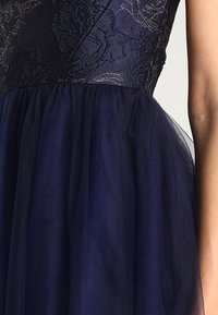 Mörkblå klänning med en texturerad bodice med blommönster och en tyllkjol som ger volym och mjukhet till den övergripande designen.