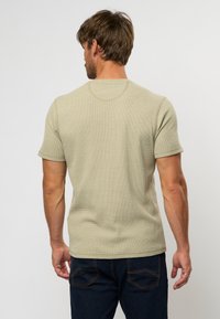 Tricou cu mânecă scurtă, de culoare verde deschis, cu textură și decolteu circular, asortat cu blugi negri cu o nuanță închisă, care au buzunare spate curbate.