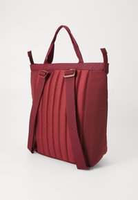 Bolsa de tela acolchada roja con dos asas y correas de hombro ajustables; presenta un diseño texturizado y una forma estructurada para la organización.