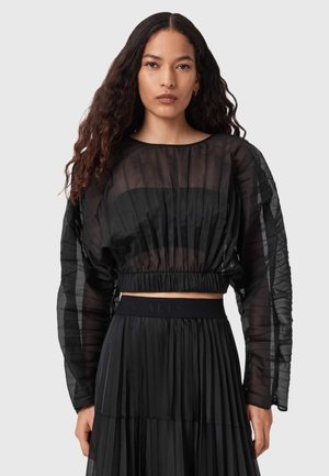 Zwarte transparante blouse met gestructureerde plooien, lange mouwen en een geplooide tailleband, gecombineerd met een bijpassende zwarte plooijrok.
