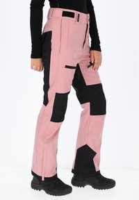 Pink and black skiing pants with a modular design, featuring zippered pockets, a wide waistband, and textured fabric for durability.