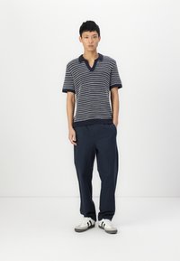 Polo tricoté bleu marine et blanc à rayures avec un design en V. Associé à un pantalon bleu marine ample et des baskets grises et blanches.