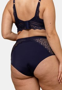 Ensemble de lingerie en dentelle bleu marine comprenant un bralette avec des bretelles ajustables et une culotte taille haute avec des accents en dentelle sur les côtés.