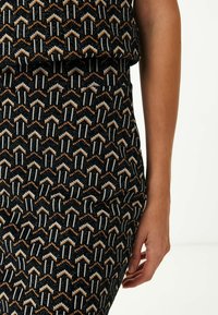 Svart mönstrad kjol med zigzag- och pilmotiv i orange, vitt och beige. Tillverkad av textilier med struktur, med en figurnära design.